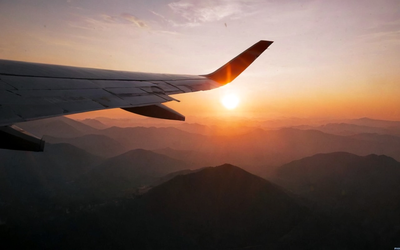Airplane wing silhouette against sunset view from airplane window